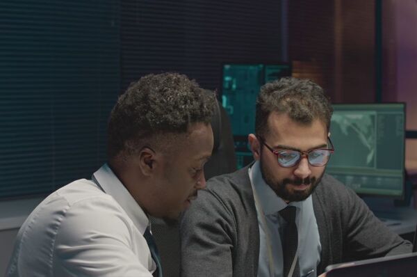waist-up-shot-of-two-multiracial-male-cybersecurity-engineers-coworking-at-night-offic-SBI-350818093-1