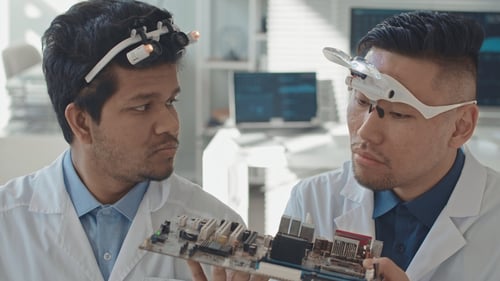 chest-up-slowmo-of-two-diverse-male-engineers-in-white-coats-examining-motherboard-poi-SBI-350773092-1
