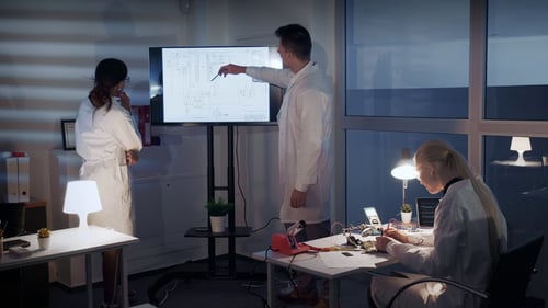 smart-team-of-electronics-development-engineers-discussing-something-on-a-big-tv-scree-SBI-350954004-1